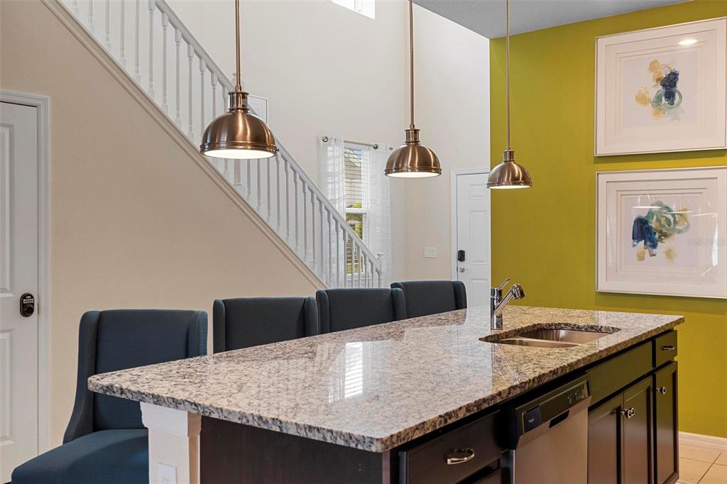 A kitchen island with granite countertops and bar stools sits before a staircase and wall — 3413 LILAC, DAVENPORT, FL