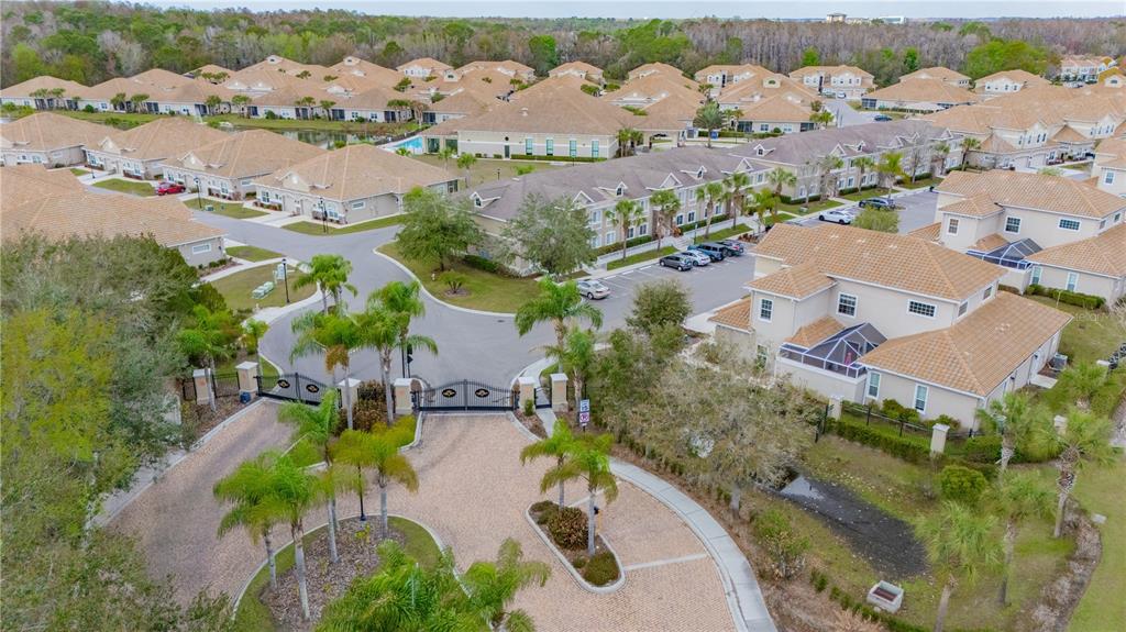 An aerial view shows a gated entrance to a residential community with numerous suburban homes — 1195 GODAVARI WAY UNIT 104, WESLEY CHAPEL, FL