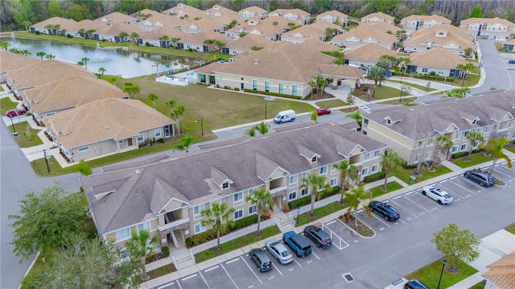 An aerial view shows a multi-story apartment complex with a parking lot and pond — 1195 GODAVARI WAY UNIT 104, WESLEY CHAPEL, FL
