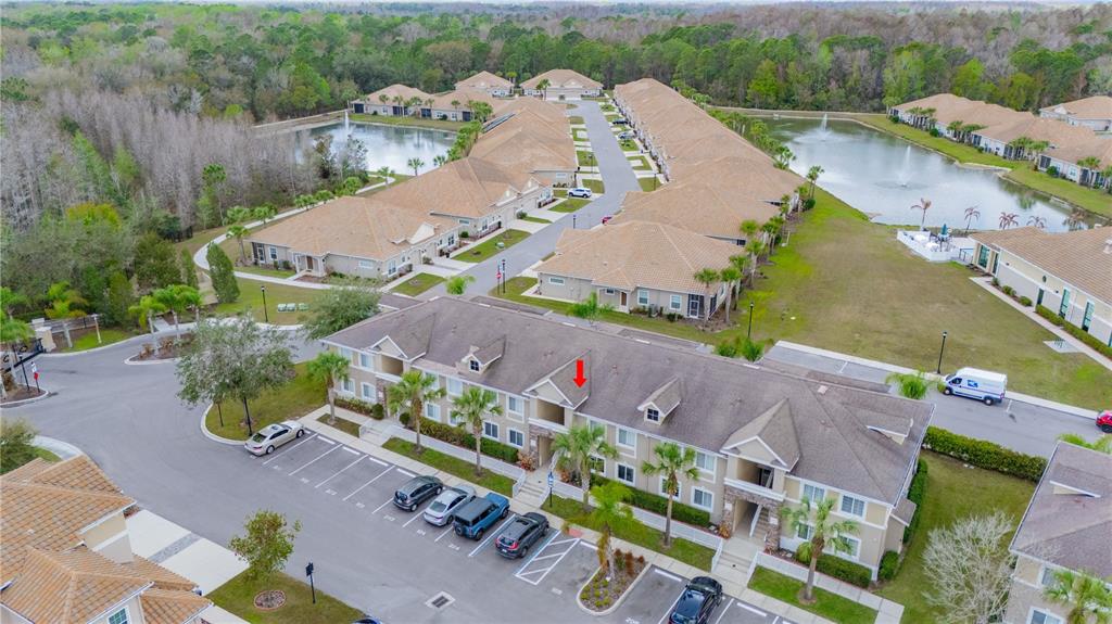 An aerial view shows a multi-story apartment building with a parking lot and nearby ponds — 1195 GODAVARI WAY UNIT 104, WESLEY CHAPEL, FL