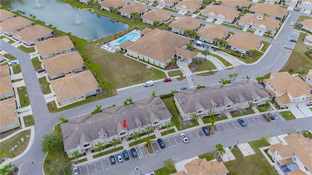 An aerial view shows a multi-unit residential building with a red arrow pointing to a balcony — 1195 GODAVARI WAY UNIT 104, WESLEY CHAPEL, FL
