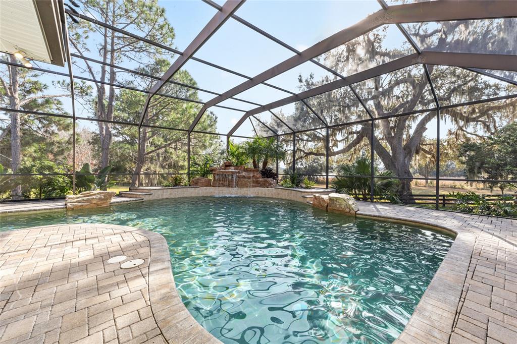 A screened-in swimming pool features a rock waterfall, stone coping, and a paver deck — 1568 BLACK LAKE DRIVE, THE VILLAGES, FL