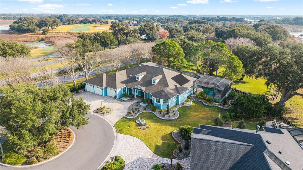 An aerial view shows a blue house with a screened pool and a paved driveway — 1568 BLACK LAKE DRIVE, THE VILLAGES, FL
