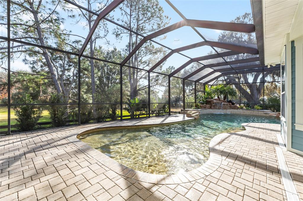 A screened-in pool area features a stone waterfall, paver decking, and views of surrounding trees — 1568 BLACK LAKE DRIVE, THE VILLAGES, FL