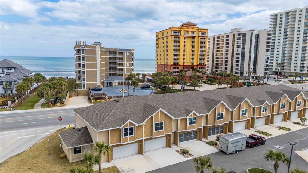 An aerial view shows a tan townhouse complex with a parking lot and nearby high-rises — 108 OCEANS CIRCLE, DAYTONA BEACH, FL
