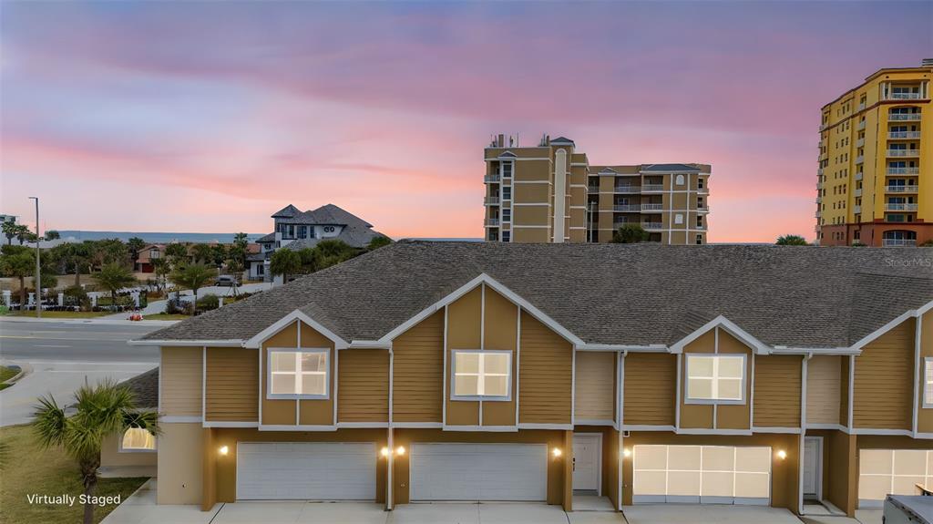 An exterior view of a multi-unit townhouse complex with attached garages at sunset — 108 OCEANS CIRCLE, DAYTONA BEACH, FL