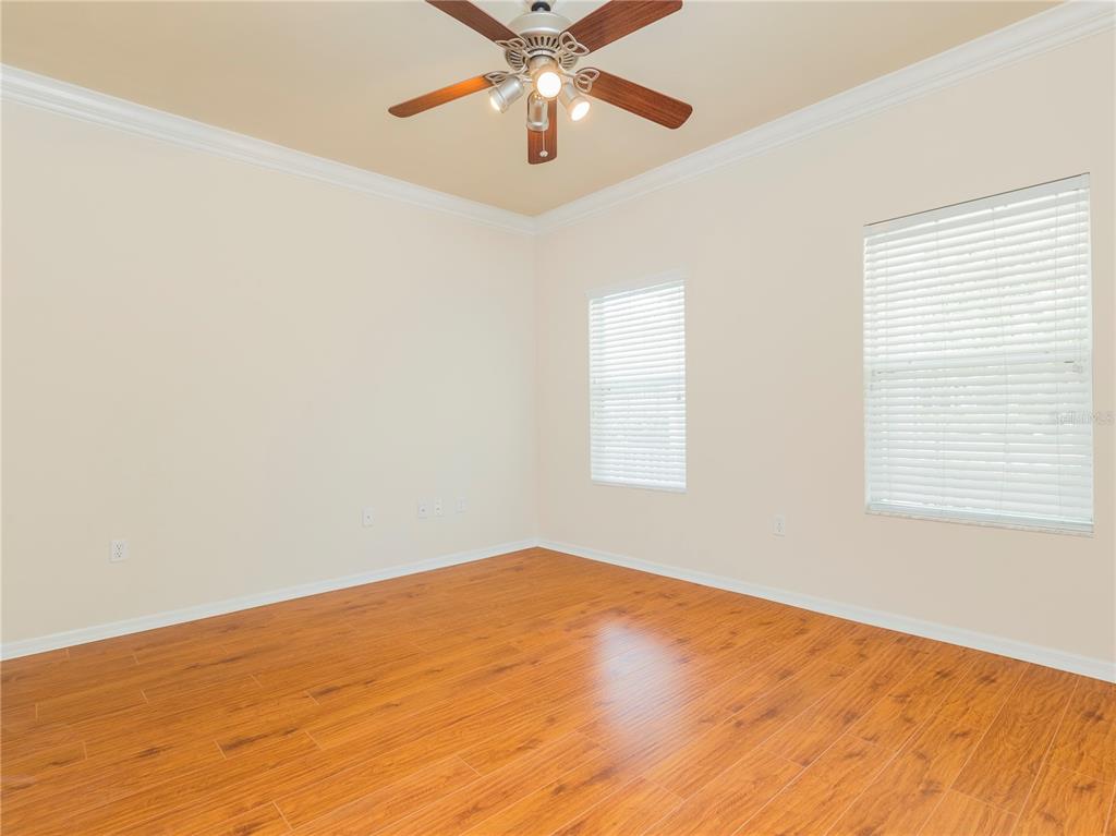 An empty room with wood-look flooring, beige walls, a ceiling fan, and two windows — 7595 SW 84TH DRIVE, GAINESVILLE, FL