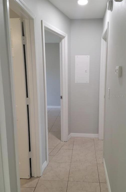 A hallway with light-colored tile flooring leads to an open doorway and a breaker panel — 783 SQUIRREL COURT UNIT B, KISSIMMEE, FL