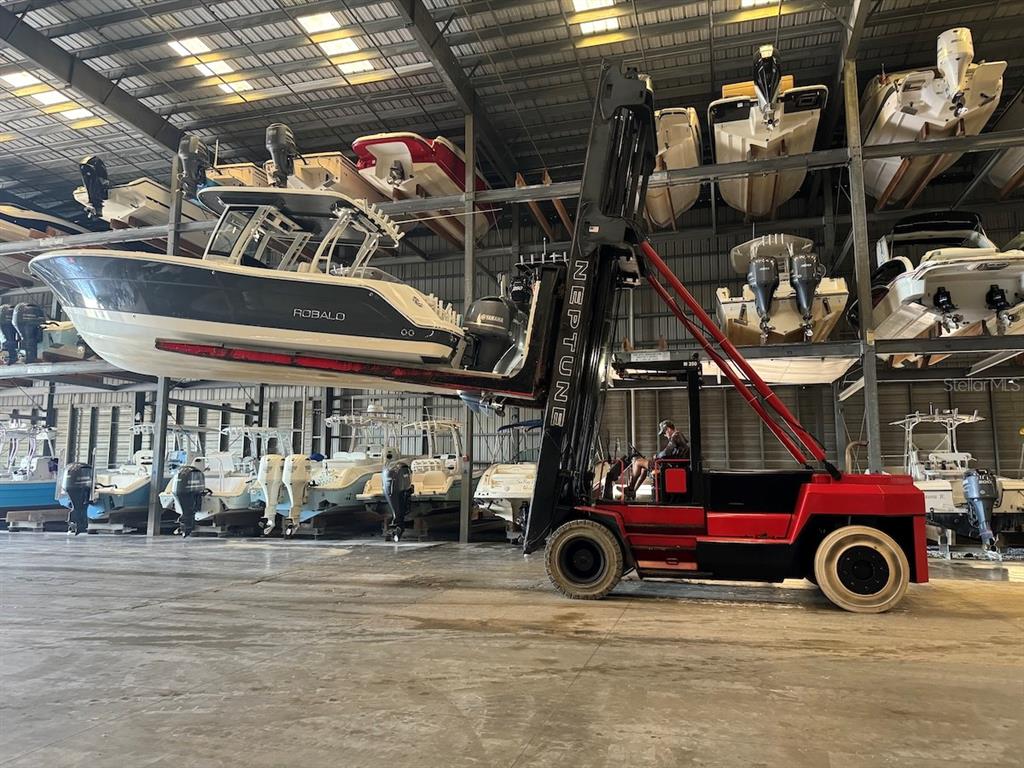A large forklift lifts a boat inside a high-ceilinged indoor boat storage facility — 1780 PHILLIPPI SHORES DRIVE UNIT F1-44, SARASOTA, FL