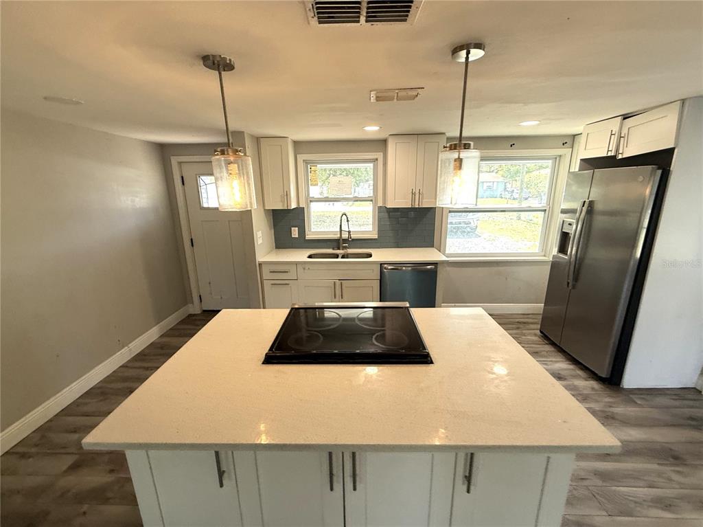 A kitchen features a central island with a cooktop, white cabinetry, and stainless steel appliances — 10015 PREVATT STREET, GIBSONTON, FL