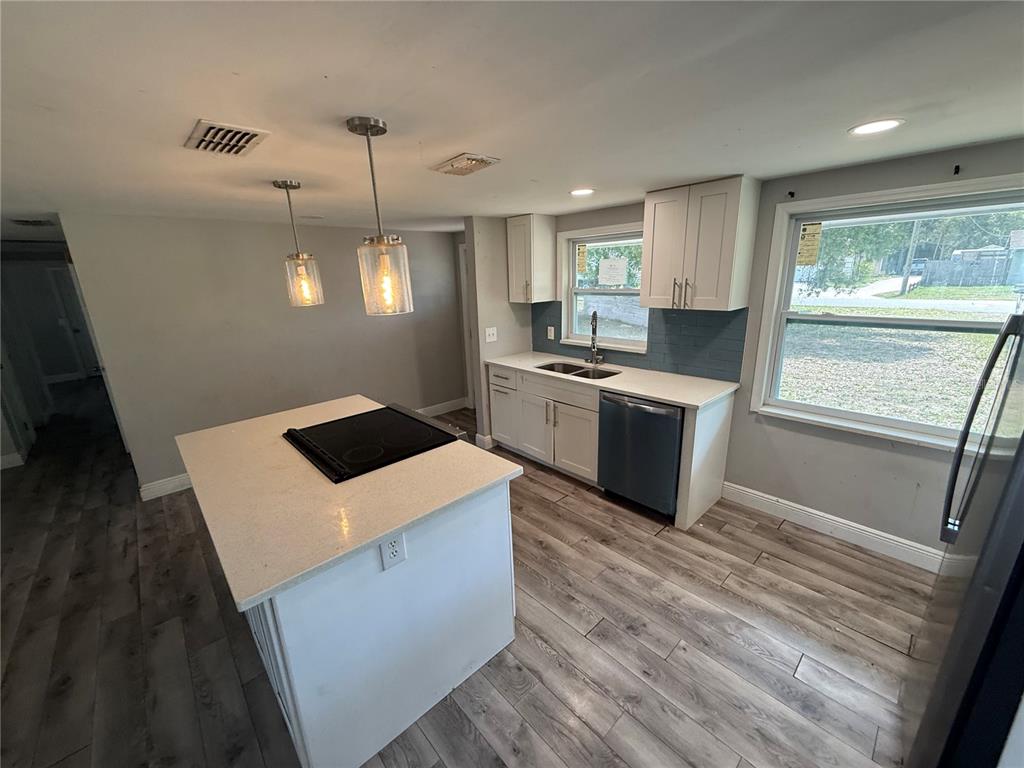 A kitchen features a central island with a cooktop, white cabinets, and wood-look flooring — 10015 PREVATT STREET, GIBSONTON, FL