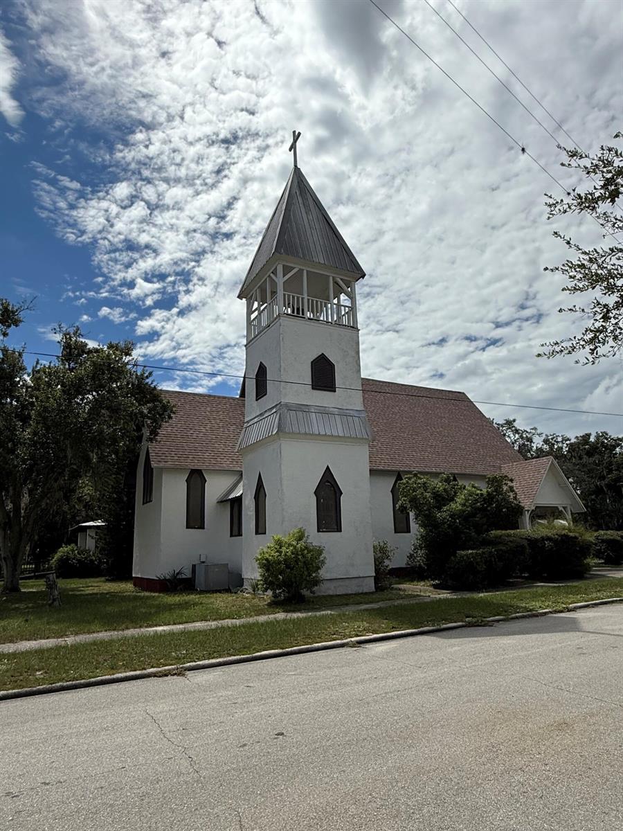 A white church with a steeple and a cross stands beside a paved street — 18 E Pleasant Street, FL 33825, FL