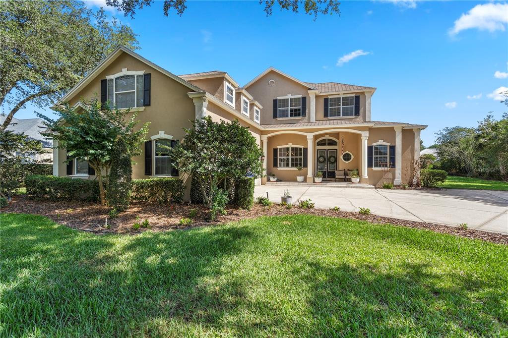A two-story suburban house with a tan stucco exterior, dark shutters, and a concrete driveway — 9527 QUEENSBURY COURT, WINDERMERE, FL