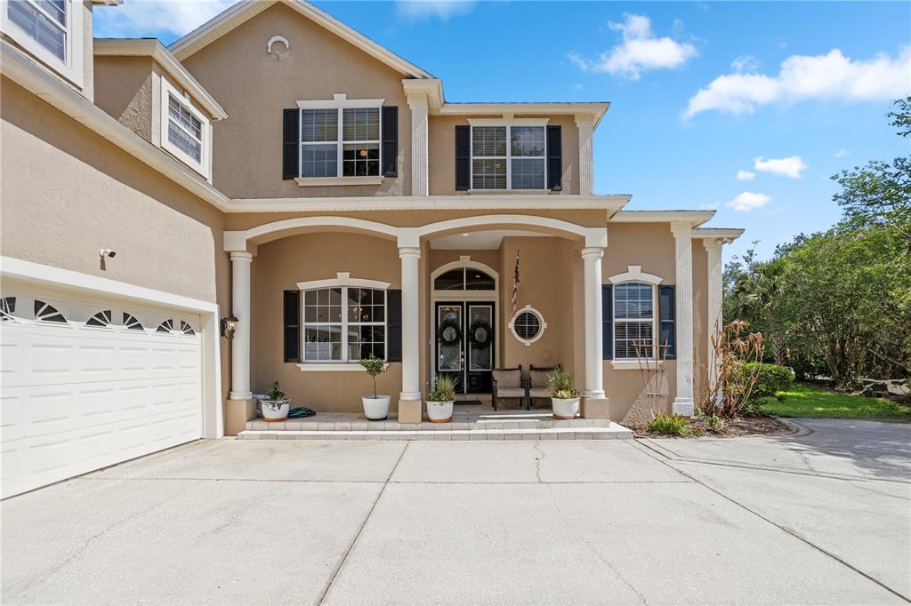 A two-story tan stucco house features a covered front porch with columns and a garage — 9527 QUEENSBURY COURT, WINDERMERE, FL
