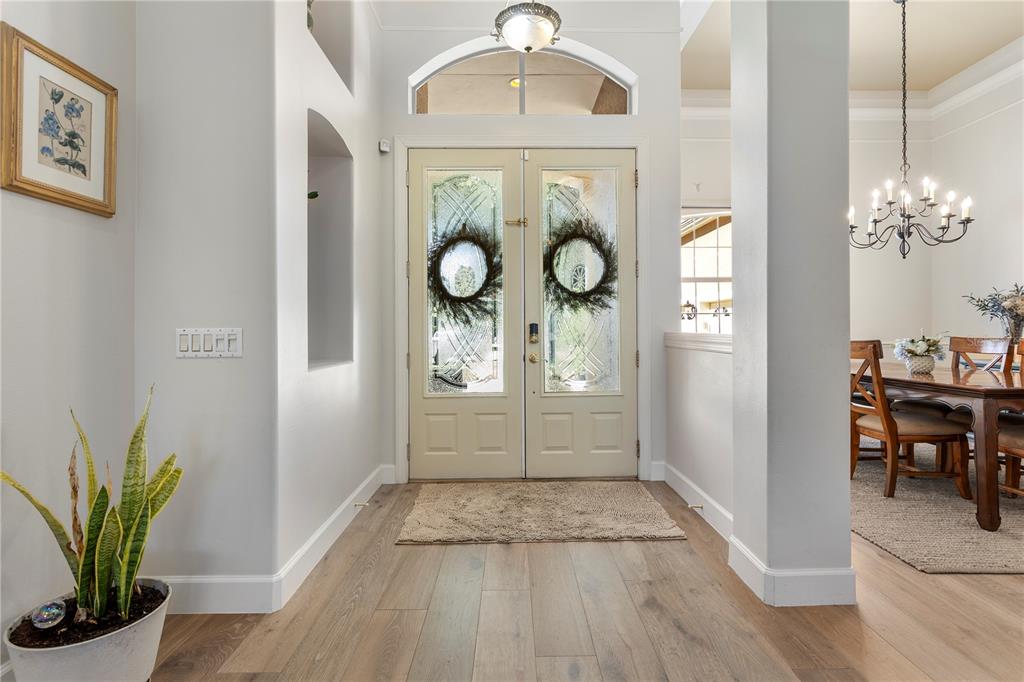 A bright entryway features light wood floors, double glass doors with wreaths, and an adjacent dining room — 9527 QUEENSBURY COURT, WINDERMERE, FL