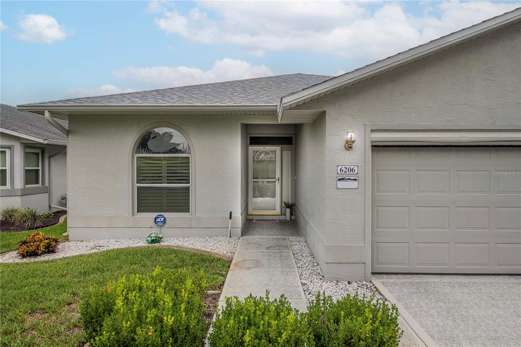 A single-story house exterior features a gray stucco facade, a garage, and a front walkway — 6206 RES CIRCLE, LAKELAND, FL
