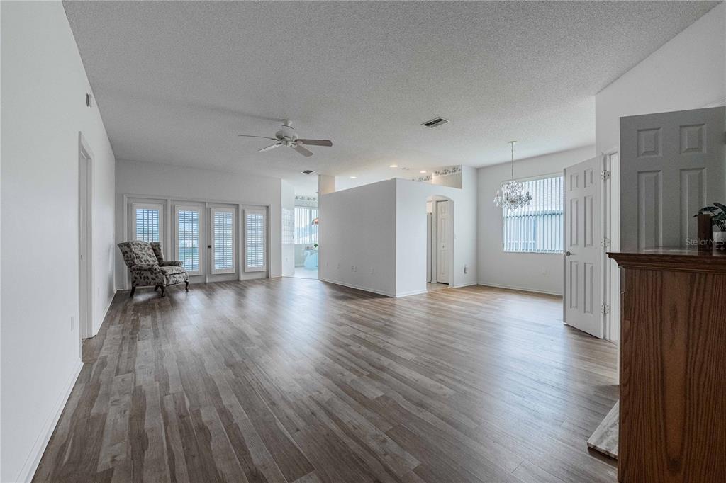 A spacious living room features light wood-look flooring, white walls, a ceiling fan, and chandelier — 6206 RES CIRCLE, LAKELAND, FL