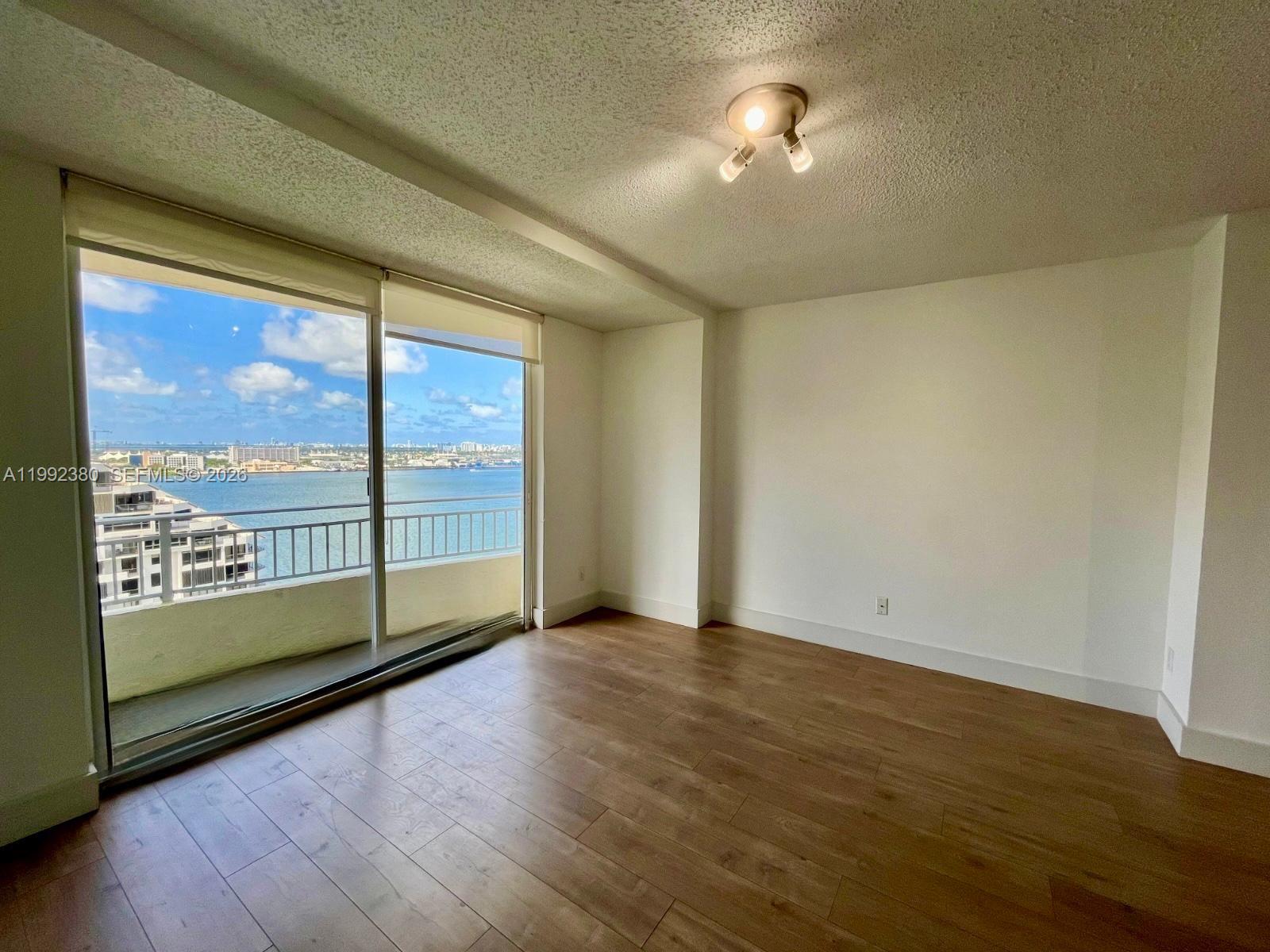 An empty room with wood-look flooring, a ceiling light, and a balcony overlooking the water — 770 Claughton Island Dr # 2009, Miami FL 33131, MIAMI, FL
