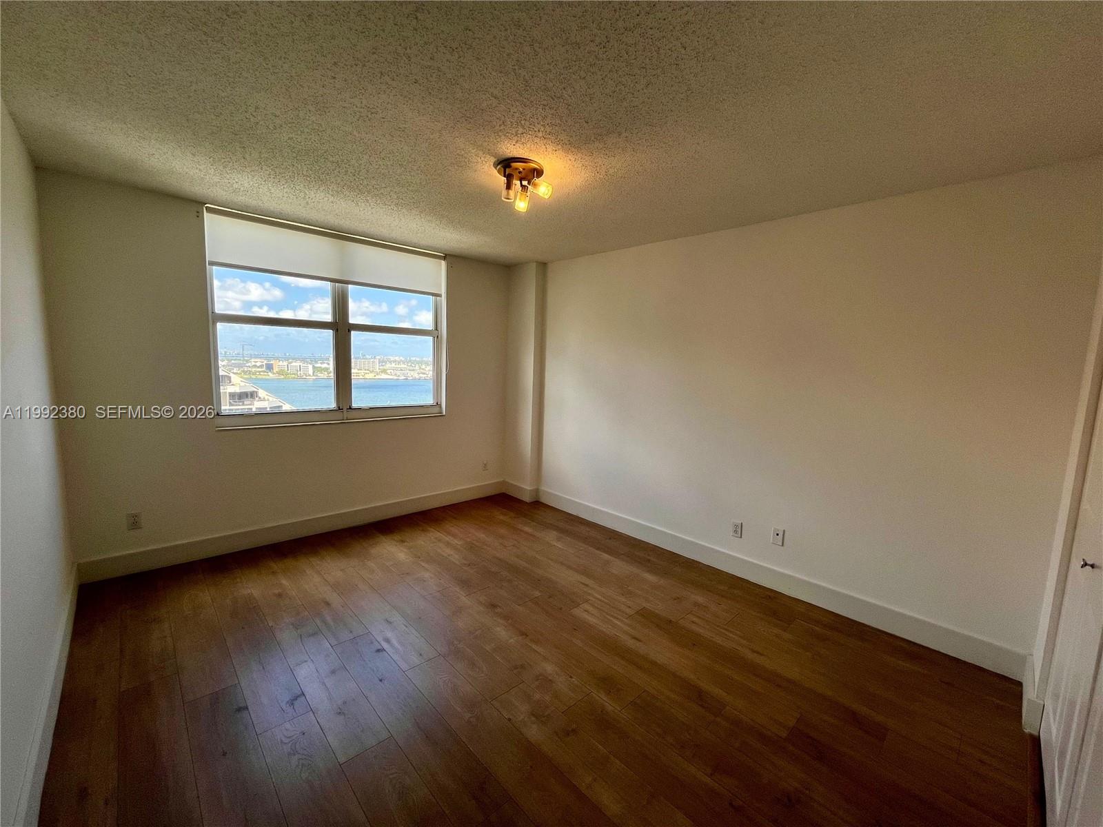 An empty bedroom features wood-look flooring, white walls, and a window with a water view — 770 Claughton Island Dr # 2009, Miami FL 33131, MIAMI, FL