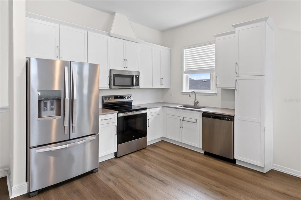 A kitchen features white cabinets, stainless steel appliances, and wood-look flooring — 10206 MEDAWAR STREET UNIT B, ORLANDO, FL