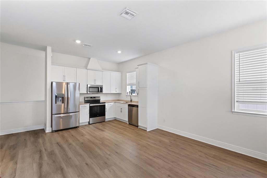 A kitchen features white cabinets, stainless steel appliances, and light wood-look flooring — 10206 MEDAWAR STREET UNIT B, ORLANDO, FL