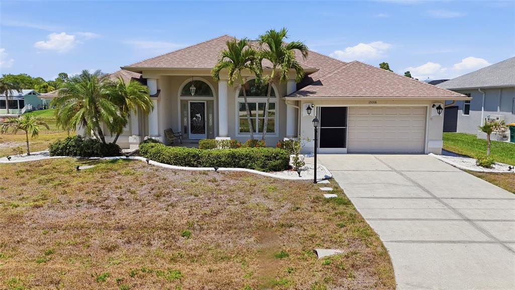 A single-story house with a beige stucco exterior, a tiled roof, and a concrete driveway — 15316 RED HEAD AVENUE, PORT CHARLOTTE, FL