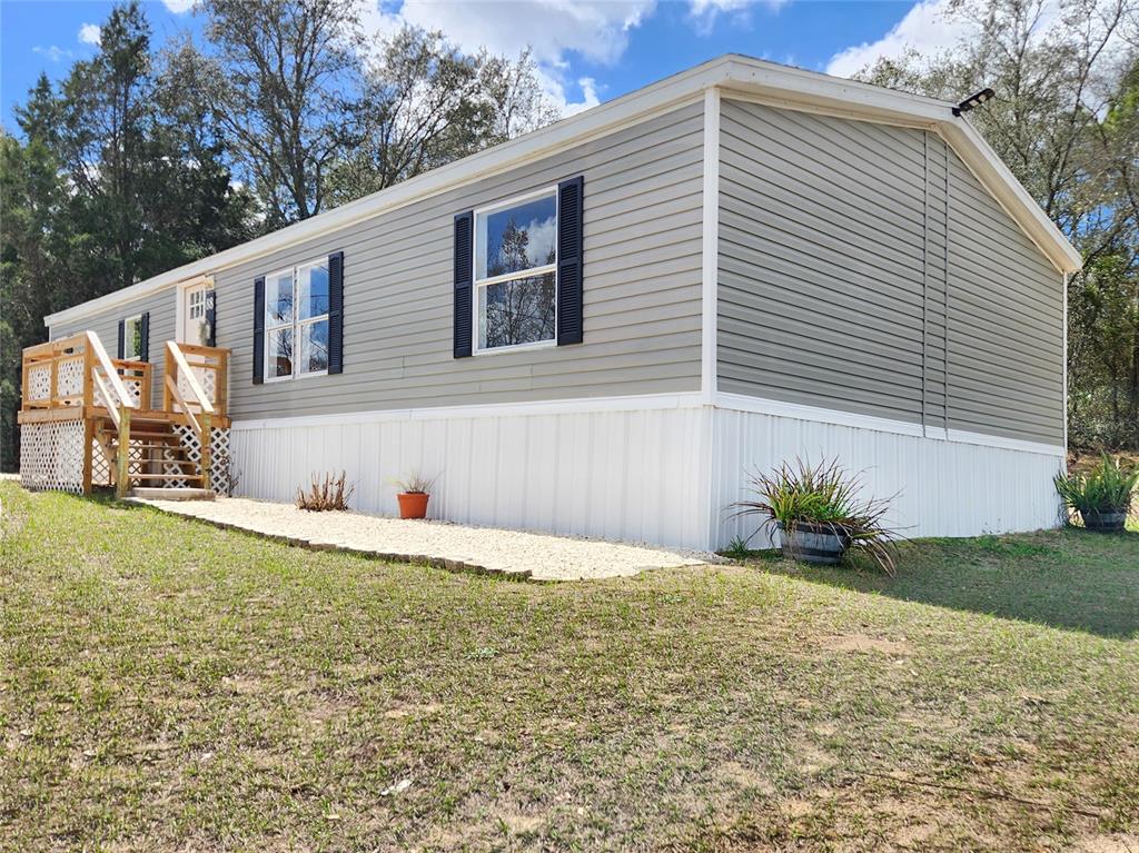 A light gray manufactured home features white skirting, black window shutters, and a wooden deck — 88 N SATURN AVENUE, INVERNESS, FL