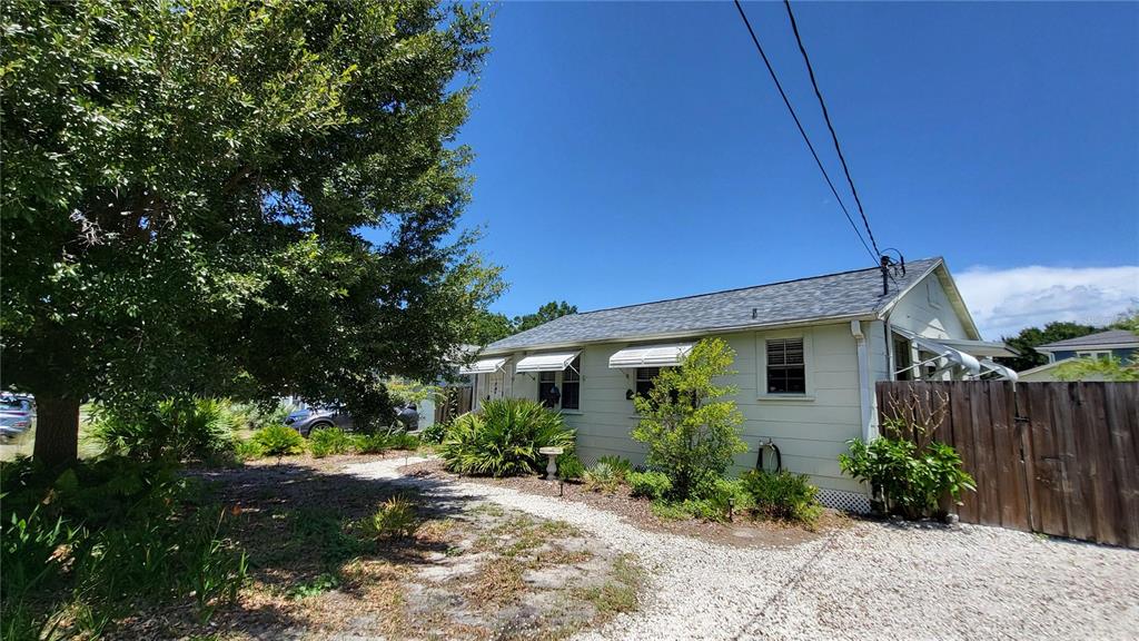 A light-colored house with a gravel driveway and a wooden fence stands under trees — 919 W WOODLAWN AVENUE, TAMPA, FL