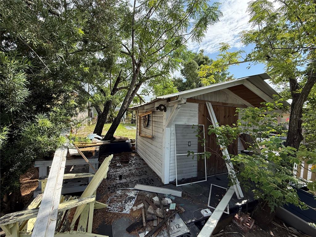 A weathered wooden shed sits in a cluttered yard surrounded by trees and debris — 2323 E 12TH AVENUE, TAMPA, FL
