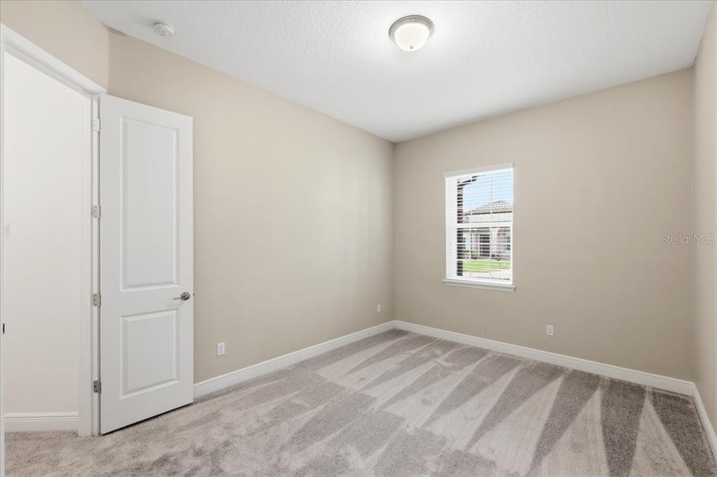 A bedroom with beige walls, gray carpet, a white door, and a single window — 16545 BROADWATER AVENUE, WINTER GARDEN, FL
