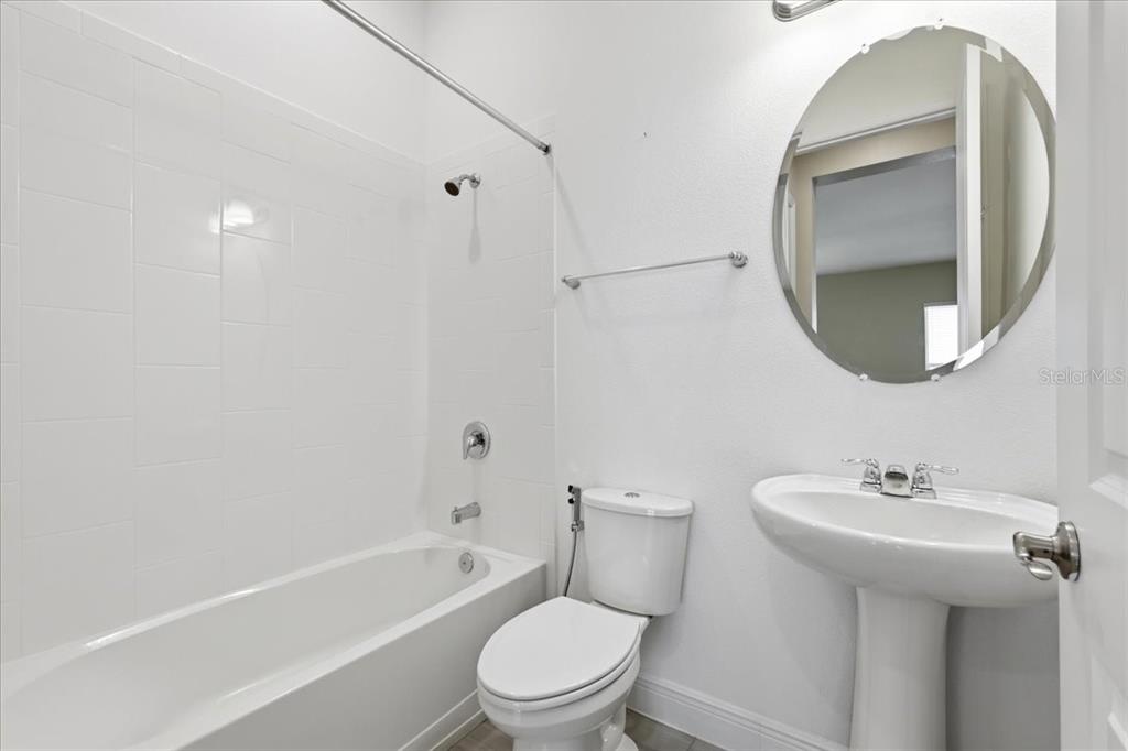 A white bathroom features a pedestal sink, a round mirror, and a shower-tub combination — 16545 BROADWATER AVENUE, WINTER GARDEN, FL