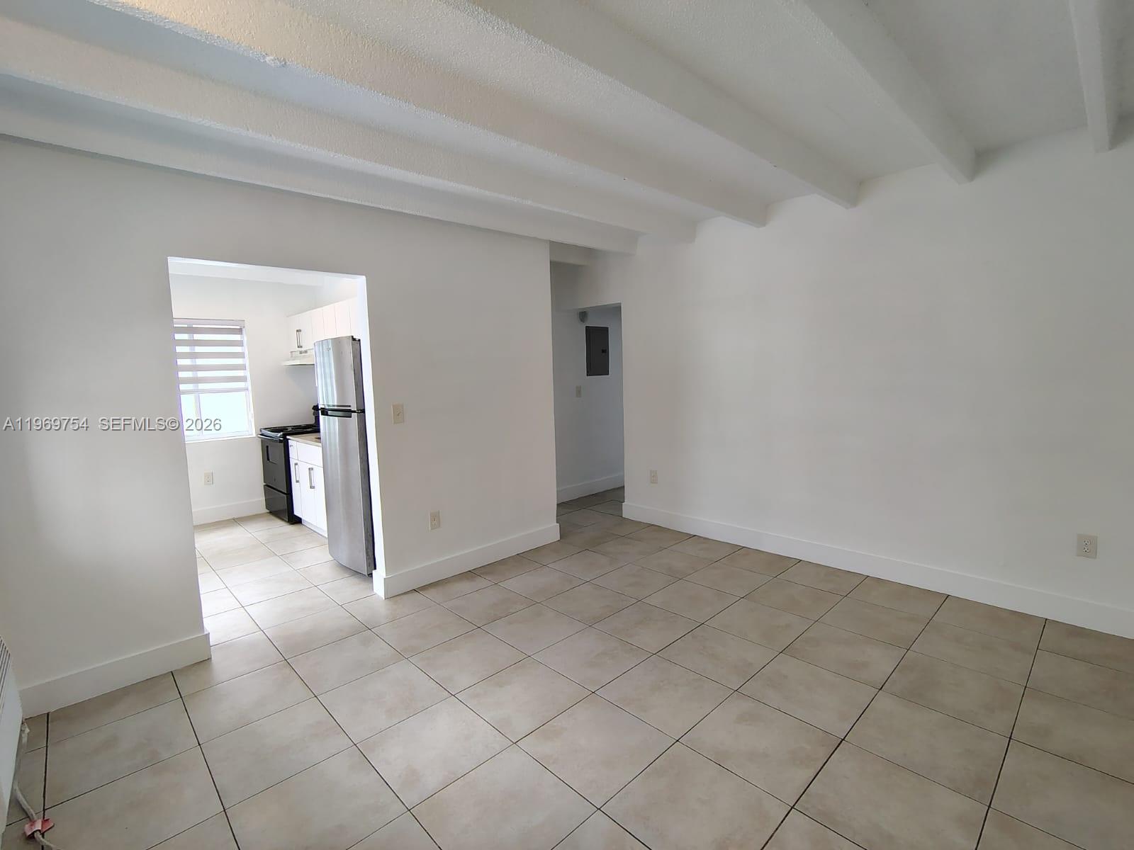 An interior view shows a tiled living area with exposed ceiling beams and an adjacent kitchen — 741 NW 60th St # 3, Miami FL 33127, MIAMI, FL