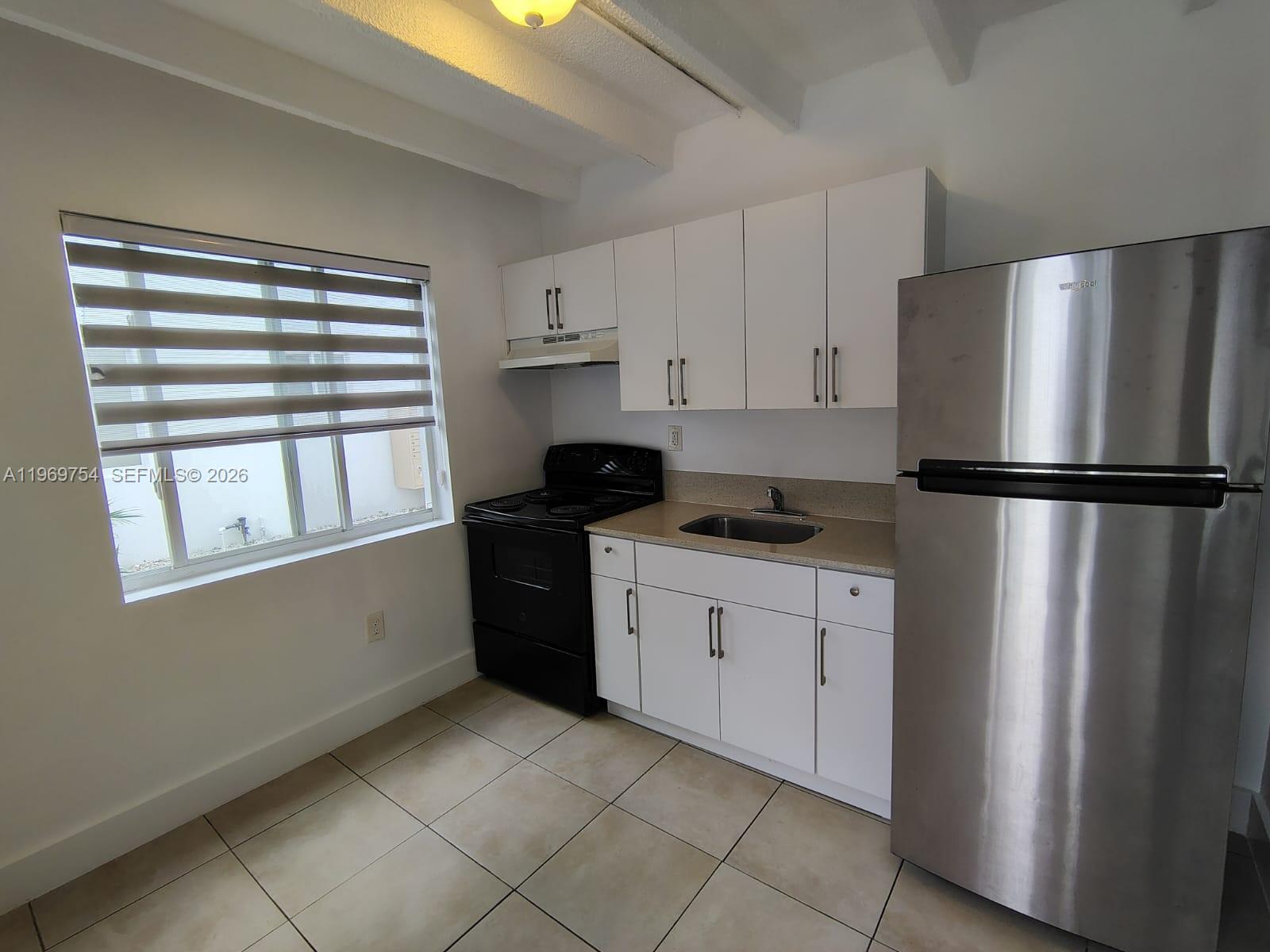 A small kitchen features white cabinets, stainless steel appliances, a black stove, and tiled floors — 741 NW 60th St # 3, Miami FL 33127, MIAMI, FL