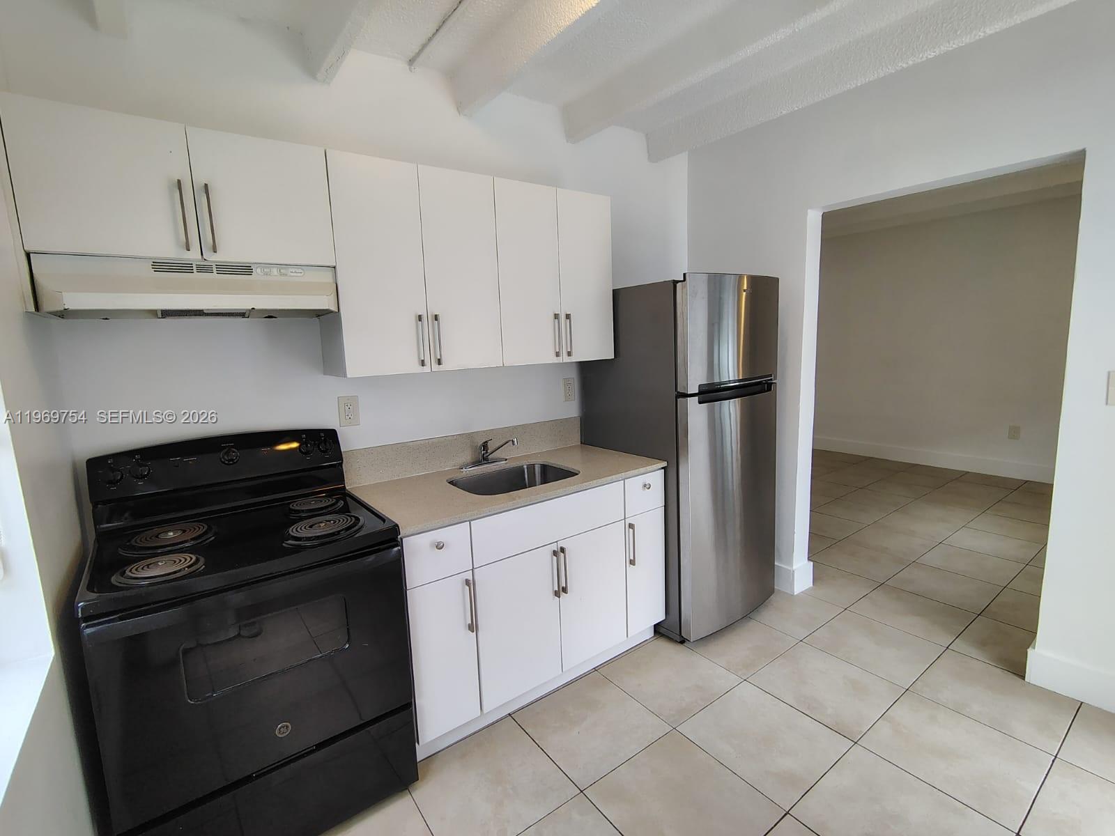 A kitchen features white cabinets, a black stove, a stainless steel refrigerator, and tiled floors — 741 NW 60th St # 3, Miami FL 33127, MIAMI, FL