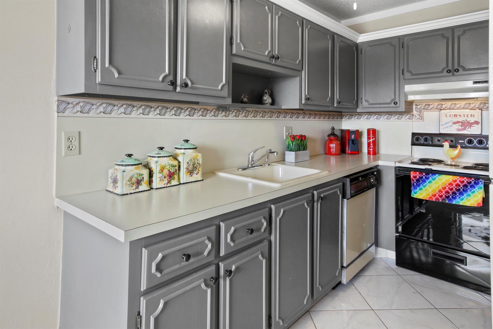 A kitchen features gray painted cabinets, white countertops, a white sink, and a black stove — 1001 Flame Vine Avenue # 202, Delray Beach FL 33445, DELRAY BEACH, FL