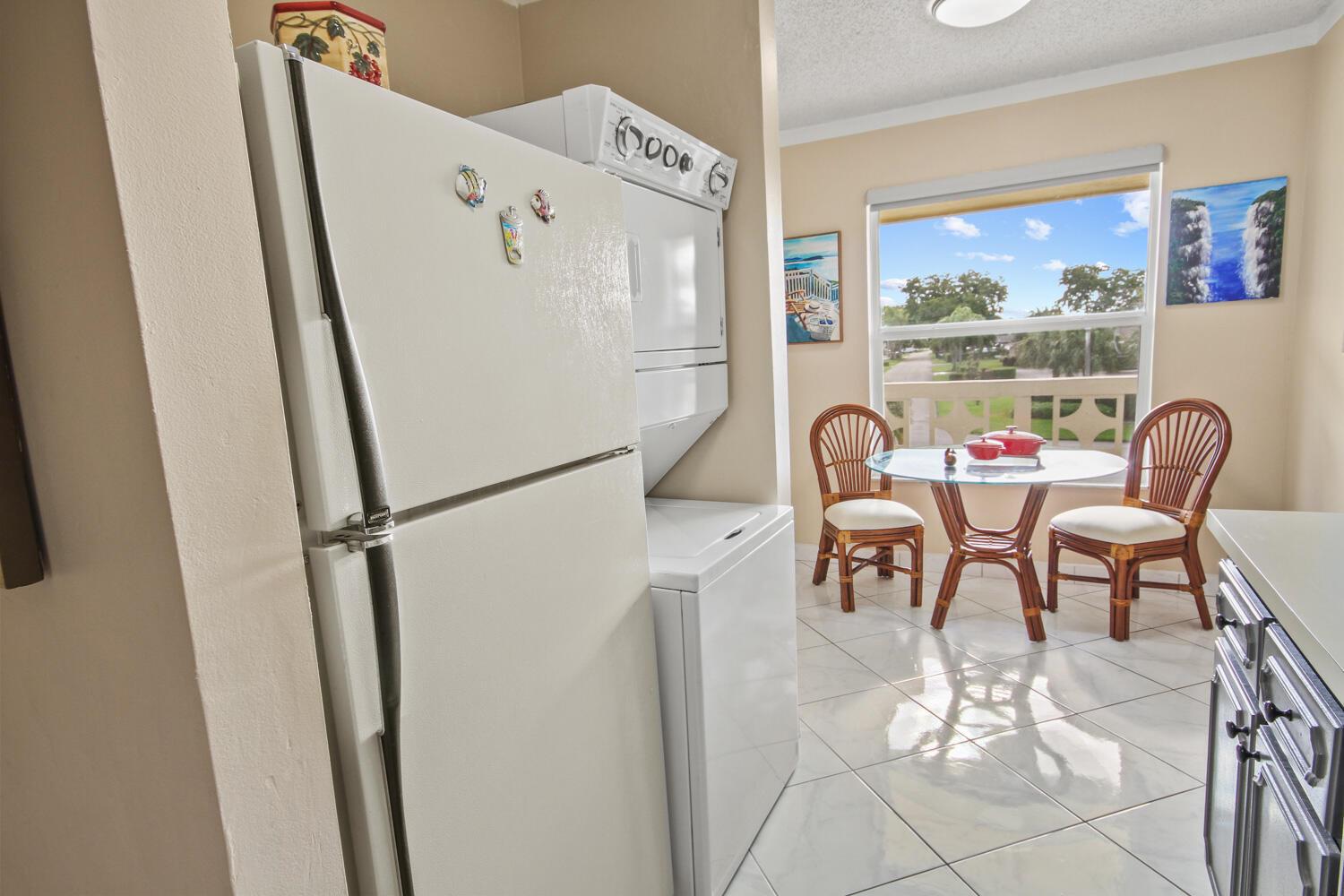 A kitchen features a white refrigerator, stacked laundry unit, and a small dining area — 1001 Flame Vine Avenue # 202, Delray Beach FL 33445, DELRAY BEACH, FL