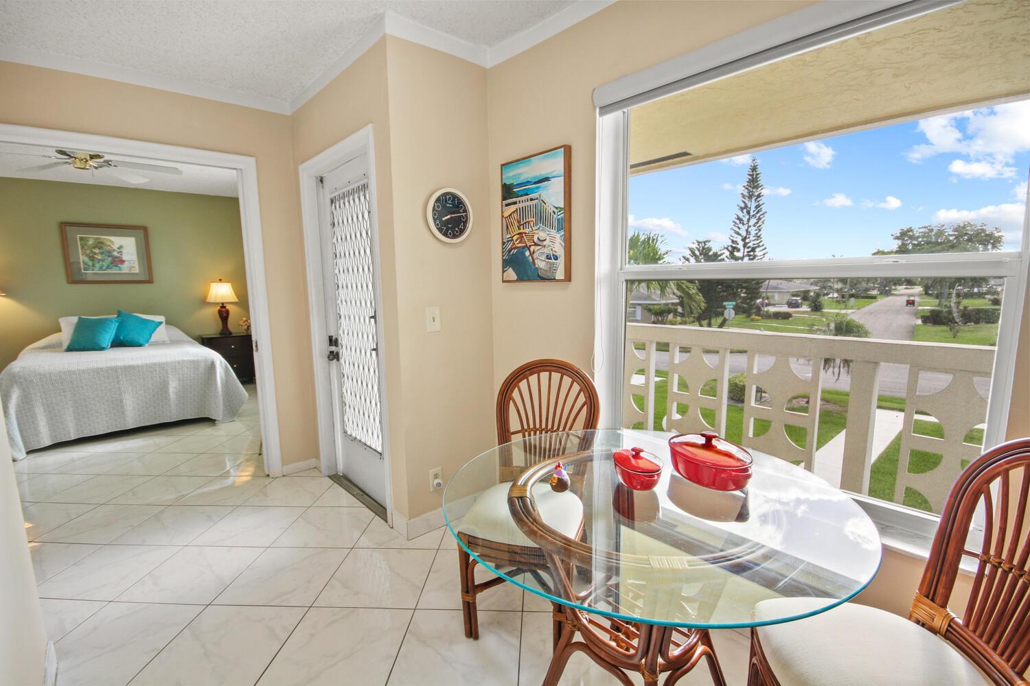A dining area with a glass table and chairs overlooks a balcony and a bedroom — 1001 Flame Vine Avenue # 202, Delray Beach FL 33445, DELRAY BEACH, FL