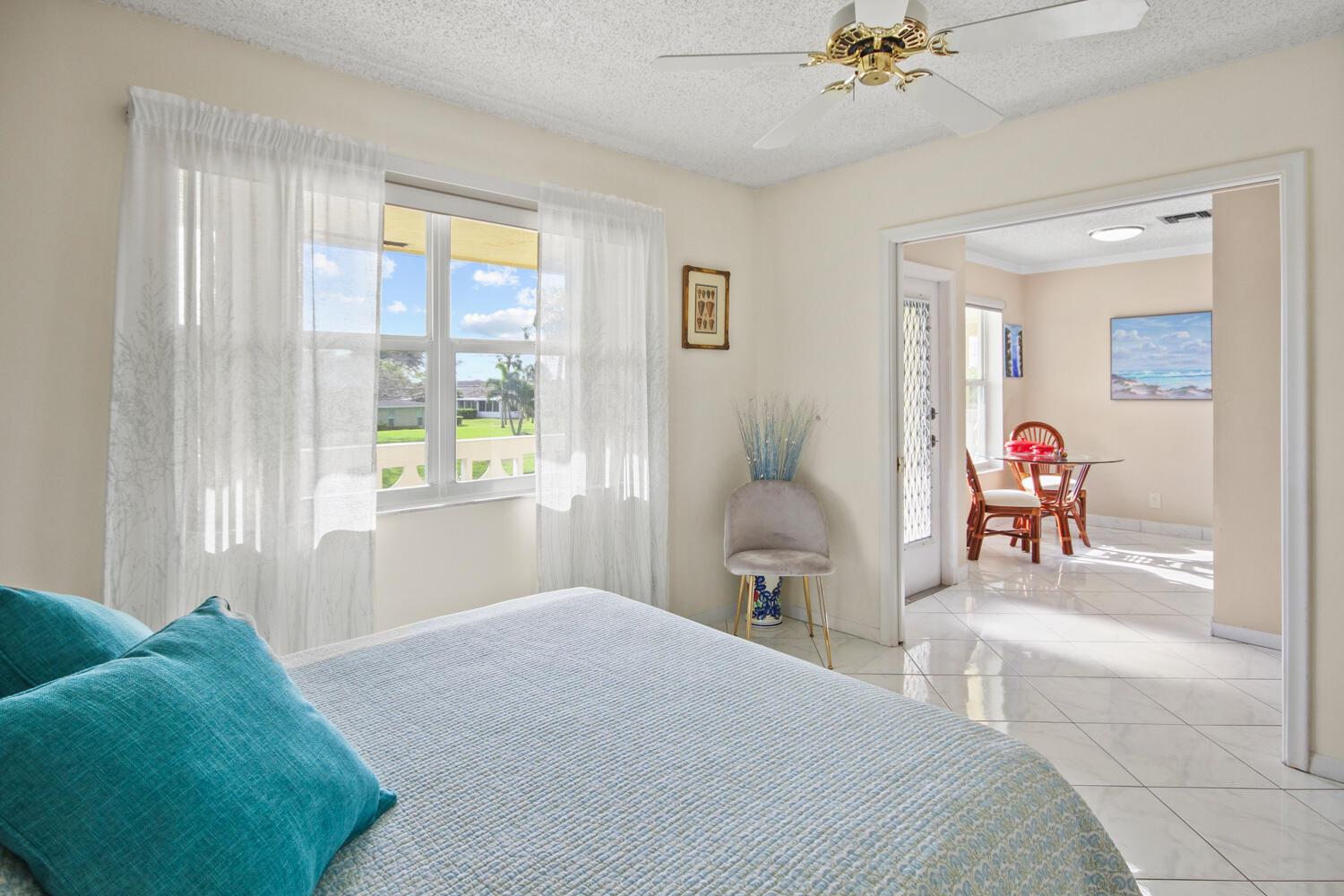 A bedroom with a bed and ceiling fan leads into a tiled dining area — 1001 Flame Vine Avenue # 202, Delray Beach FL 33445, DELRAY BEACH, FL