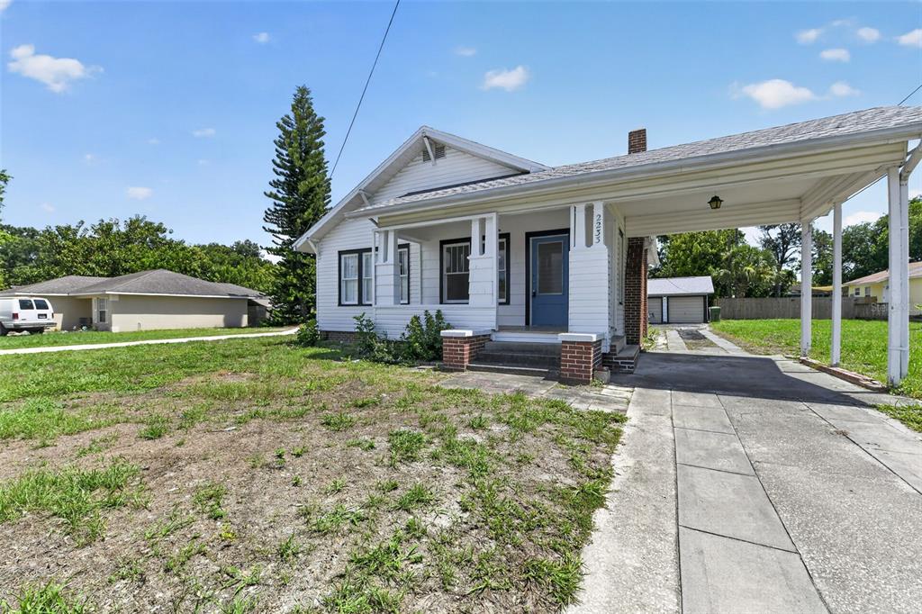 A white house with a front porch and an attached carport sits on a lawn — 2233 11TH AVENUE W, BRADENTON, FL