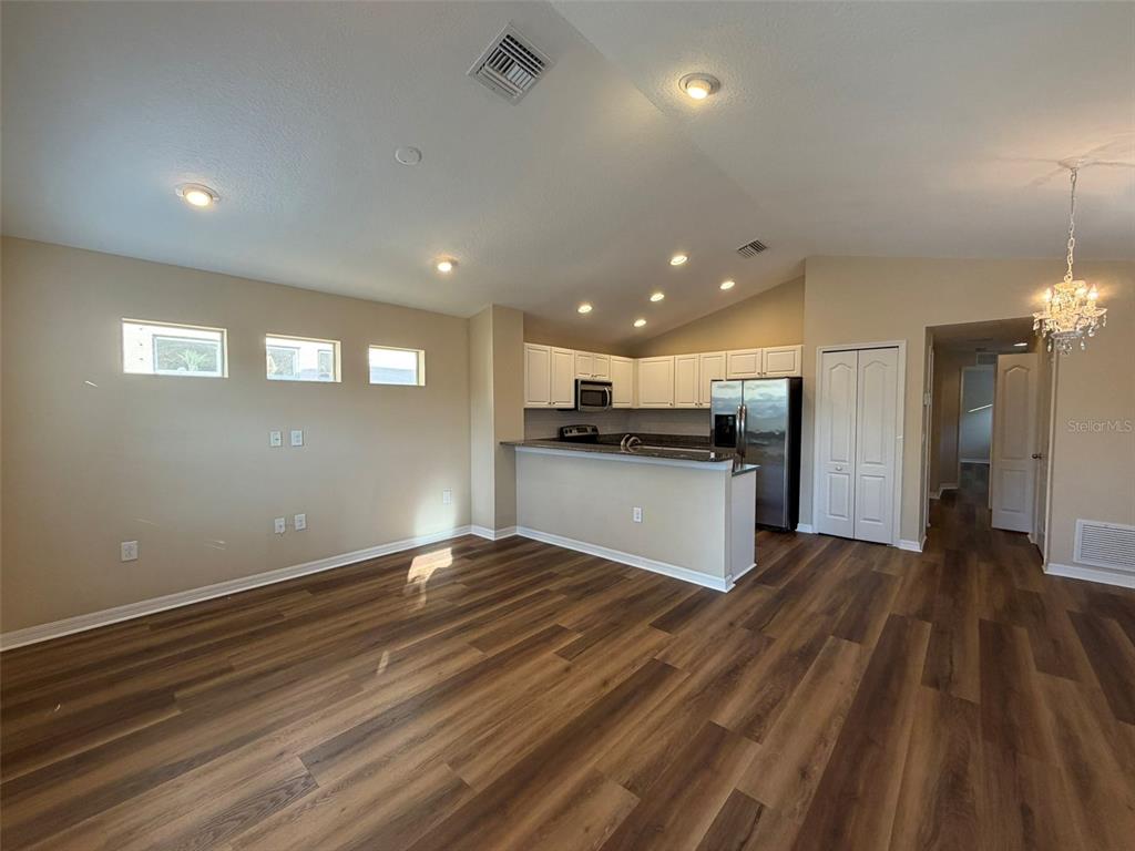 An open-concept living area features wood-look flooring, a kitchen with white cabinets, and recessed lighting — 4735 WOODBROOK DR, SARASOTA, FL