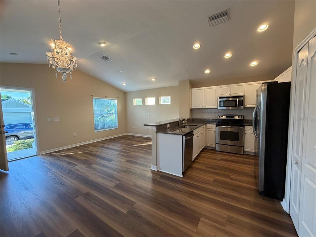 An open-concept kitchen and living area features wood-look flooring, white cabinets, and stainless appliances — 4735 WOODBROOK DR, SARASOTA, FL