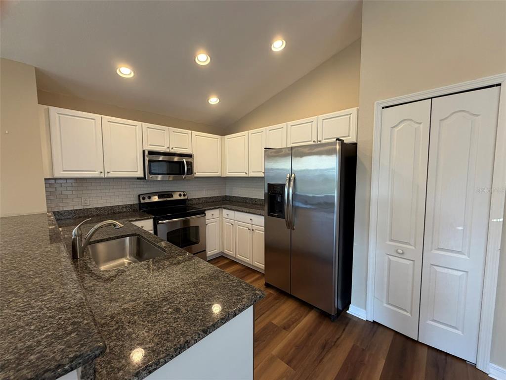 A kitchen features white cabinets, granite countertops, stainless steel appliances, and wood-look flooring — 4735 WOODBROOK DR, SARASOTA, FL