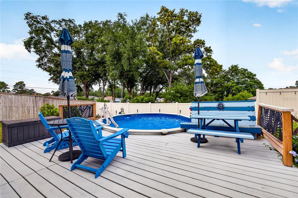 A backyard deck features a round above-ground pool, blue patio furniture, and two striped umbrellas — 8501 SE 160TH PLACE, SUMMERFIELD, FL