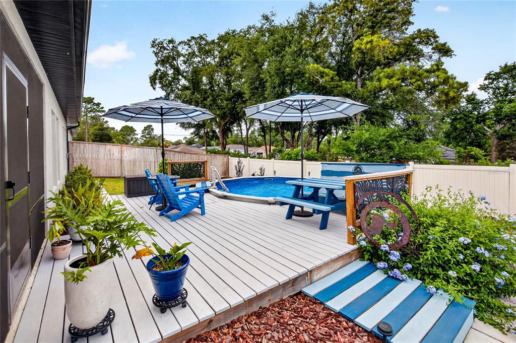 A backyard deck features a swimming pool, blue patio furniture, and two striped umbrellas — 8501 SE 160TH PLACE, SUMMERFIELD, FL