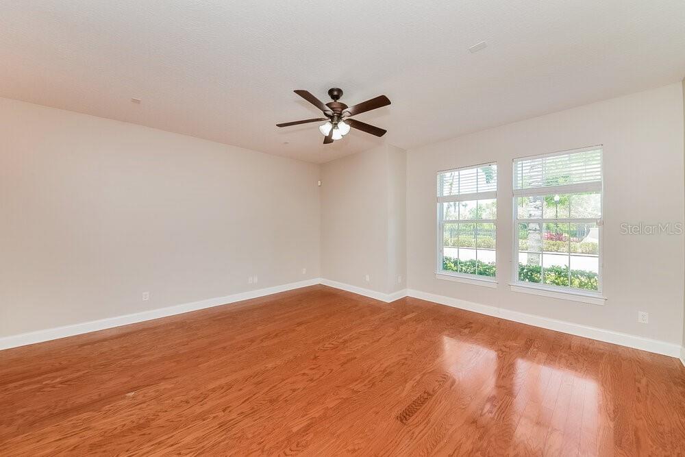 An empty room features hardwood floors, a ceiling fan, and two windows with white trim — 204 ABERDEEN POND DRIVE, APOLLO BEACH, FL