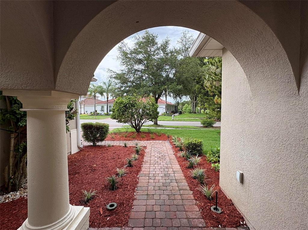 A paved walkway leads through a landscaped yard under a covered arched entryway — 3700 PARADISO CIRCLE, KISSIMMEE, FL