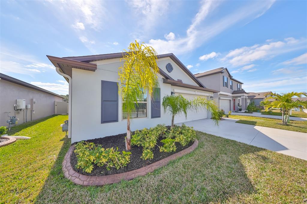 A single-story house with a white stucco exterior, dark shutters, and a landscaped front yard — 9316 CHANNING HILL DRIVE, RUSKIN, FL