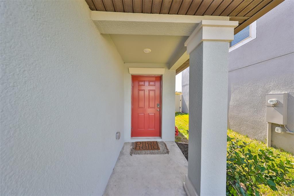 A covered entryway features a red front door, a concrete porch, and a support column — 9316 CHANNING HILL DRIVE, RUSKIN, FL