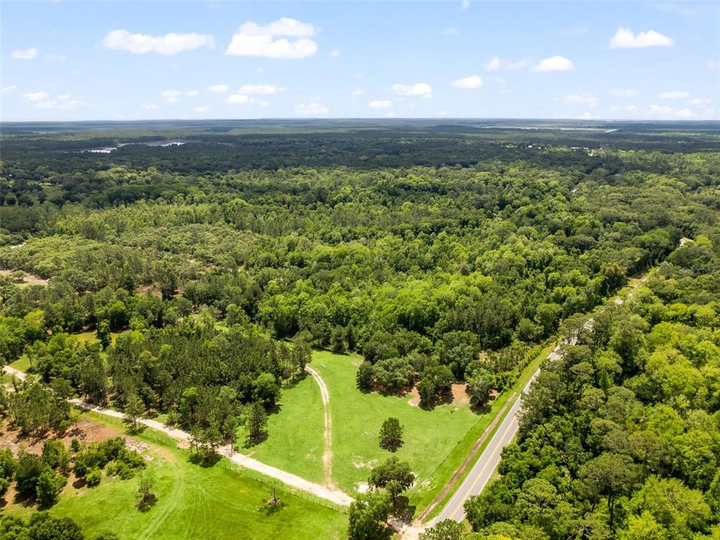 An aerial view shows a rural landscape with a paved road, open pasture, and forest — 0 SE 182ND AVENUE SE, OCKLAWAHA, FL