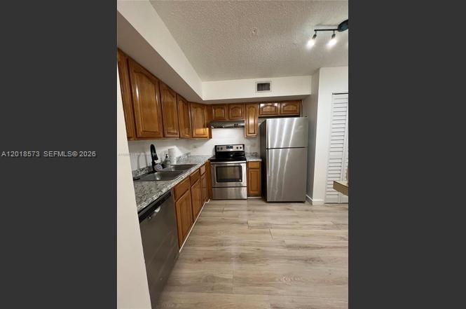 A kitchen features wooden cabinets, stainless steel appliances, and light-colored wood-look flooring — 3700 N 56th Ave # 1012, Hollywood FL 33021, HOLLYWOOD, FL